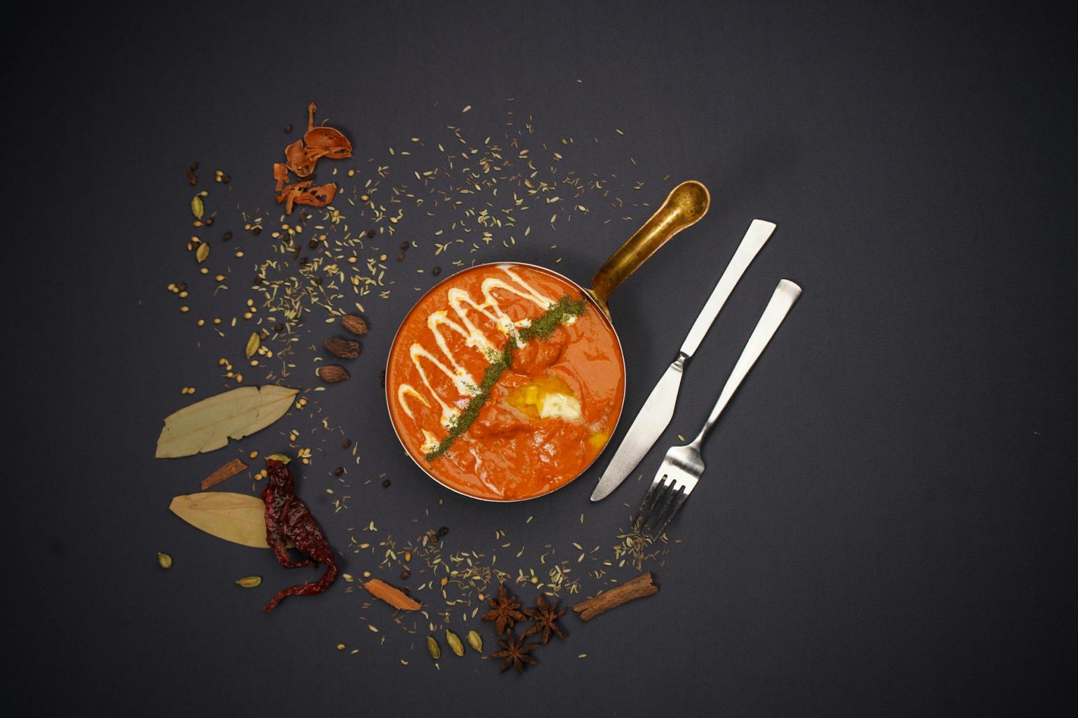 Top view of Indian curry with spices and cutlery on dark background. Perfect for food lovers.