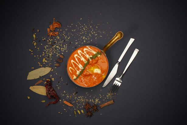 Top view of Indian curry with spices and cutlery on dark background. Perfect for food lovers.