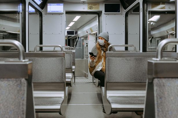 A woman wearing a face mask is sitting alone on a nearly empty urban train, practicing safety measures.