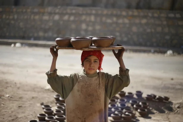 A child craftsman in Cairo carrying handmade pottery outdoors.