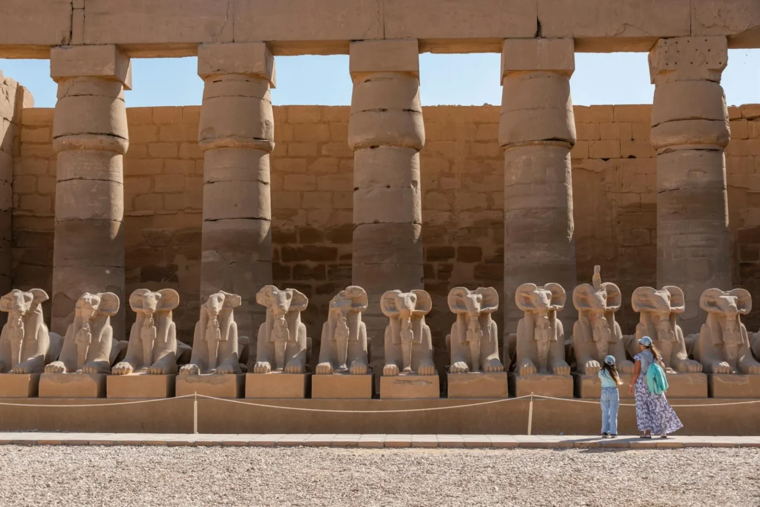 A view of the ram-headed sphinx statues at Karnak Temple Complex with visitors exploring the site.