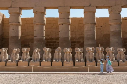 A view of the ram-headed sphinx statues at Karnak Temple Complex with visitors exploring the site.