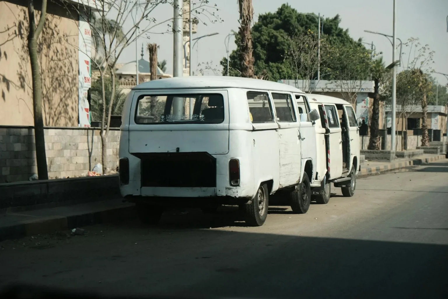 Rustic vintage vans parked in a row on a leafy Cairo street, depicting local transport.