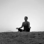 A woman practices meditation on the beach at sunset, embracing tranquility and relaxation.