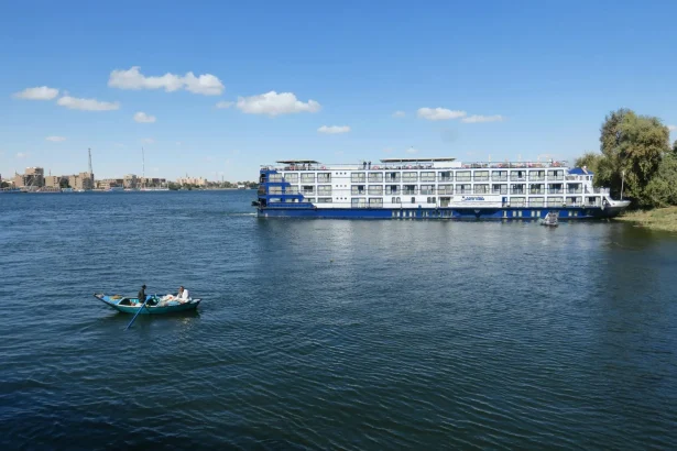A ferry boat and rowboat on the Nile River under a clear blue sky in Luxor, Egypt.