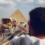 Tourists enjoy horse-drawn carriages near the iconic Giza pyramids on a sunny day.