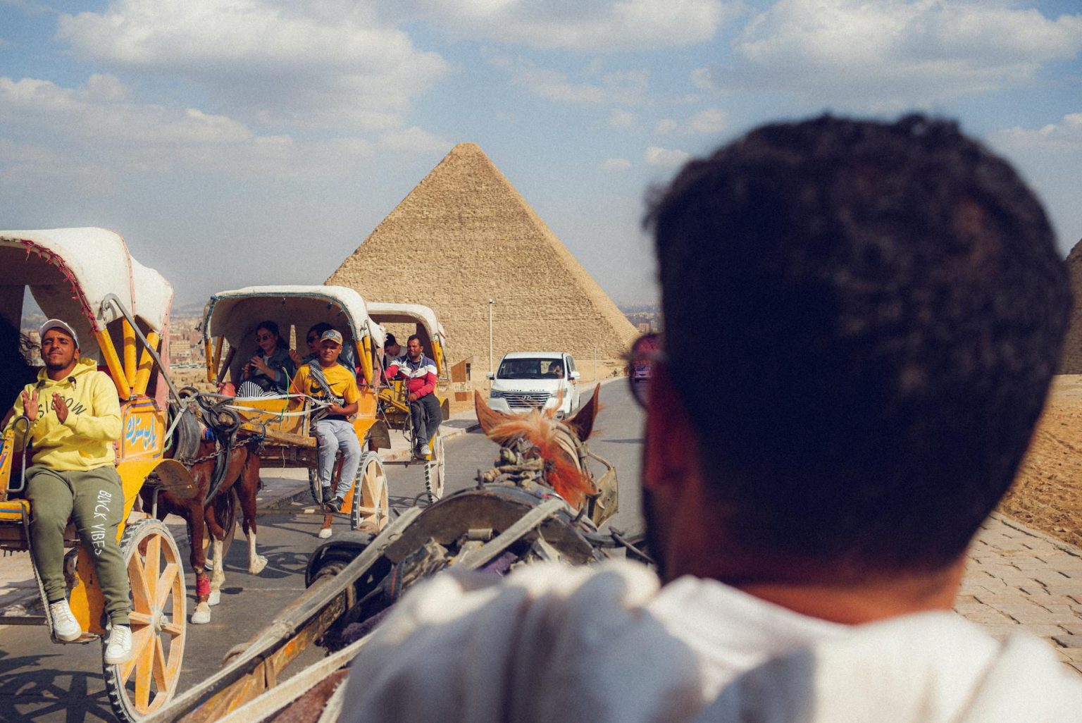 Tourists enjoy horse-drawn carriages near the iconic Giza pyramids on a sunny day.