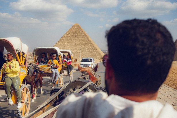 Tourists enjoy horse-drawn carriages near the iconic Giza pyramids on a sunny day.