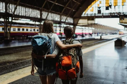 Backpackers waiting at a train station, embracing with arm around shoulders.