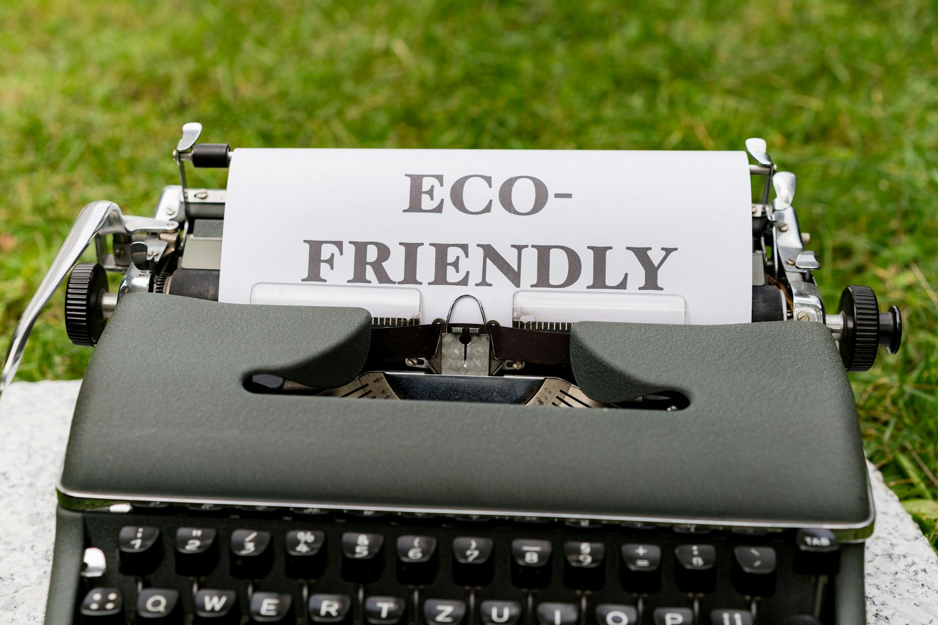 A vintage typewriter displays an eco-friendly message outdoors on grass.
