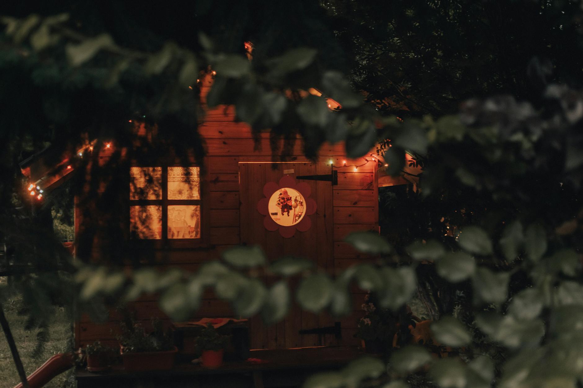 A charming treehouse illuminated at night with soft, warm lighting and surrounded by lush foliage.