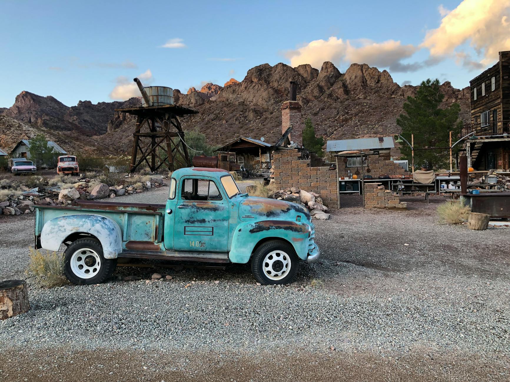 Aged turquoise truck in a desert ghost town with mountains in the background, capturing the Wild West ambiance.