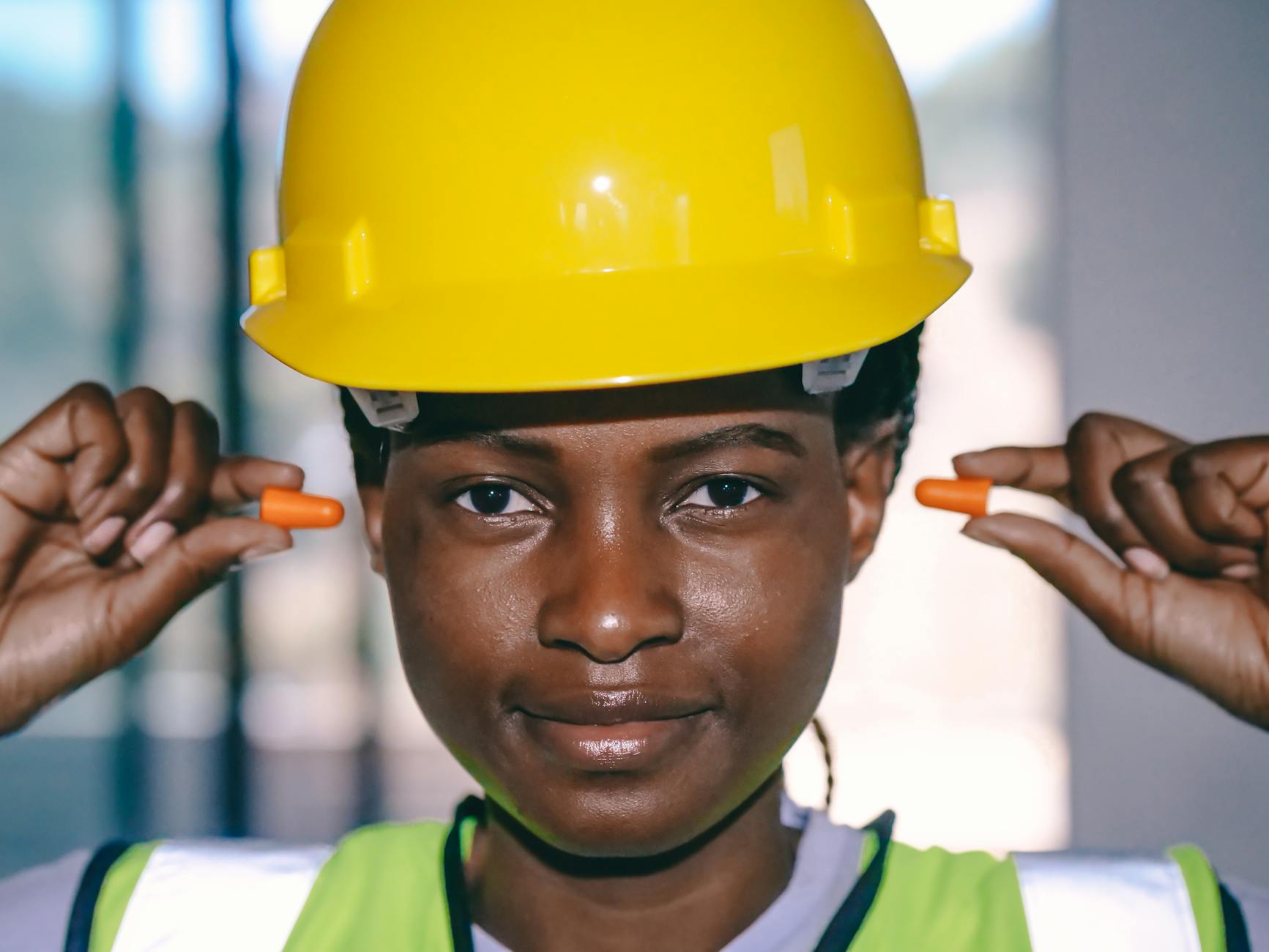 Close-up of an African American woman in safety gear wearing ear protection at work.