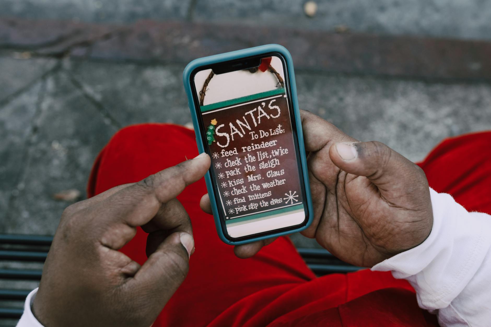 Close-up of hands holding a smartphone displaying Santa's whimsical to-do list outdoors.