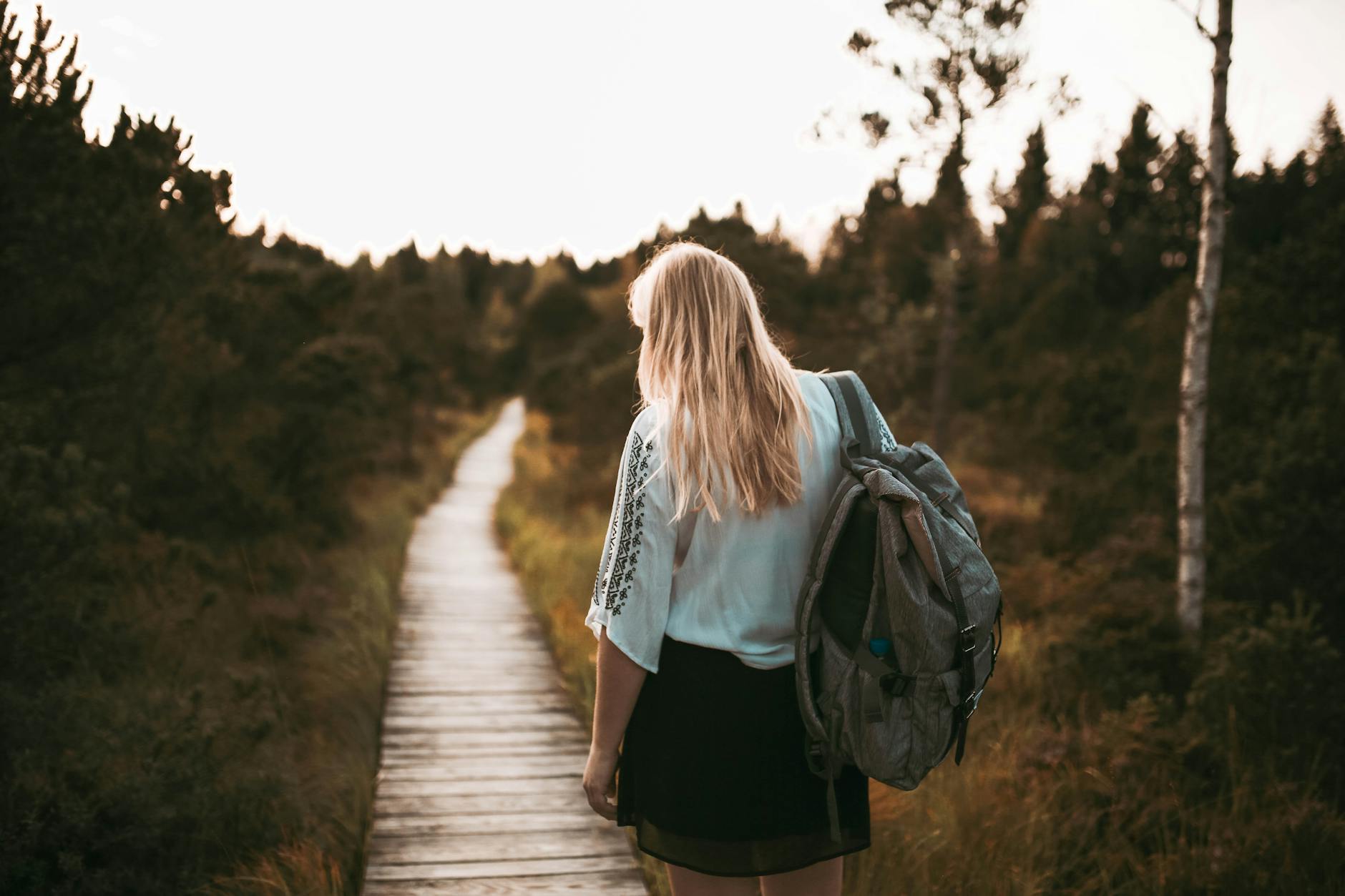 A woman with a backpack enjoys a peaceful walk on a forest boardwalk at sunset.