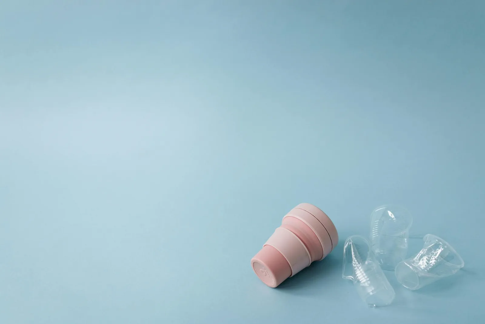 A reusable silicone cup next to crushed plastic cups on a blue background, promoting sustainability and zero waste.