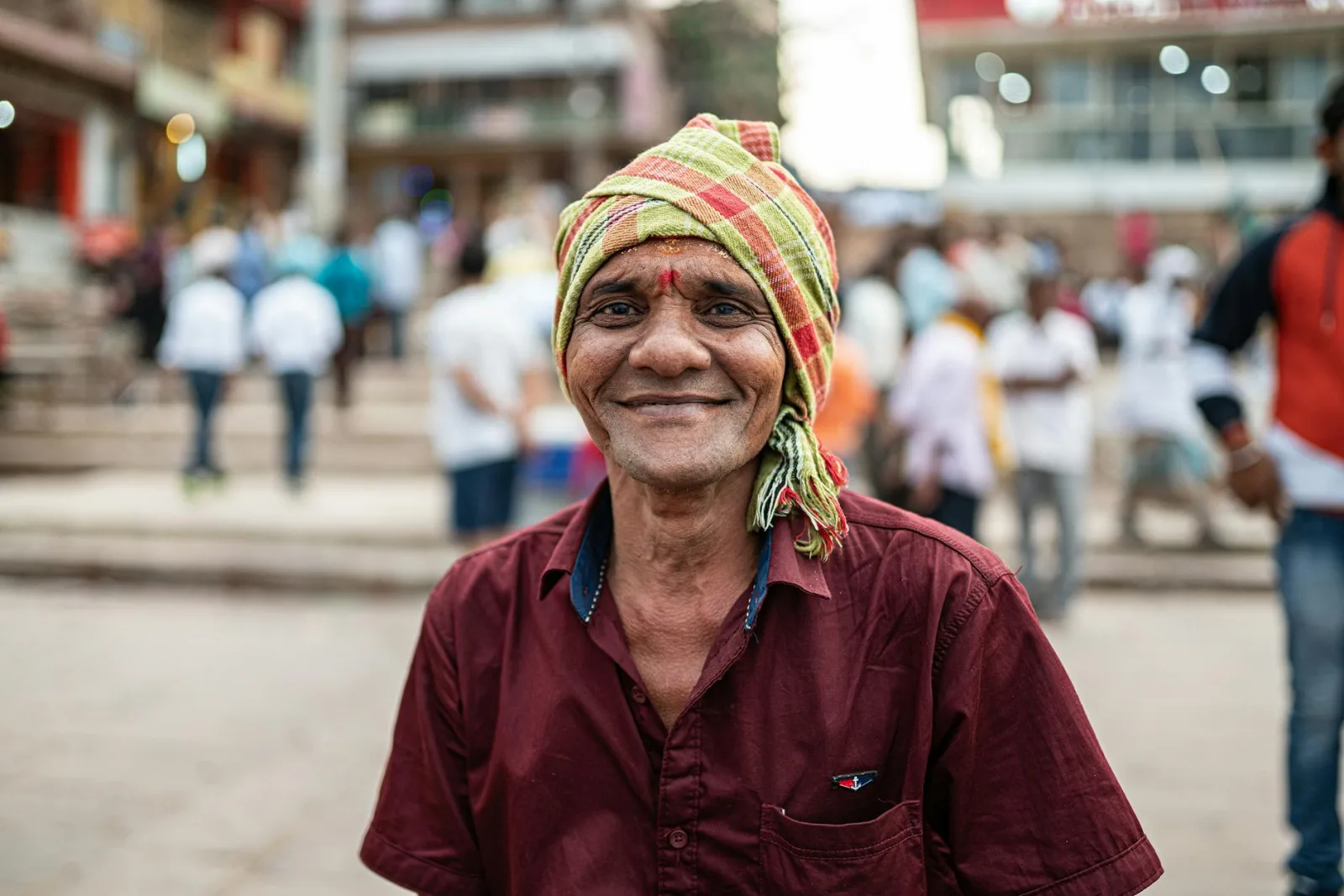 A joyful man in traditional attire smiles warmly in a bustling Varanasi street.