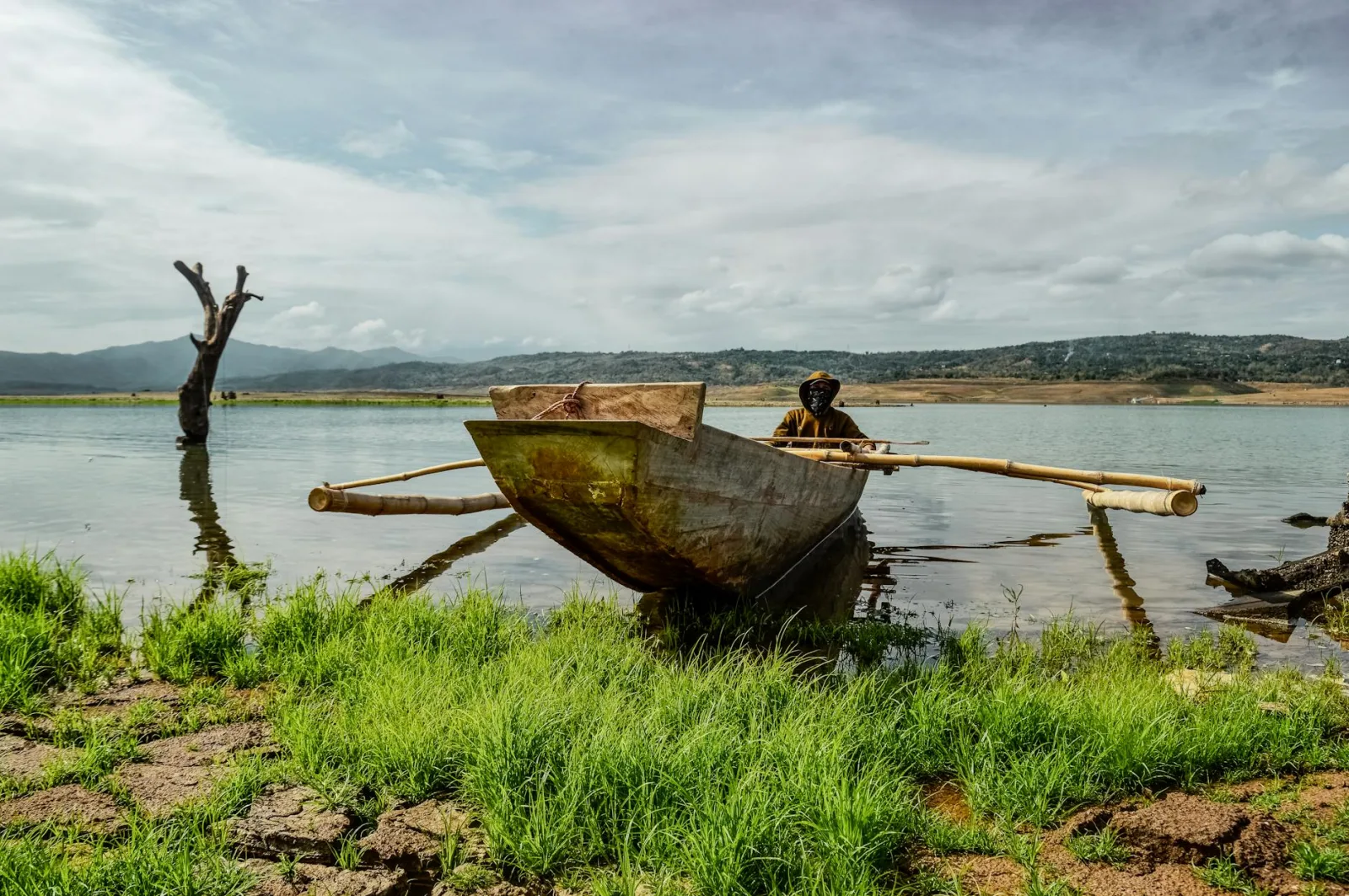 A traditional fisherman in an outrigger boat on Pantabangan Lake with scenic mountainous backdrop.