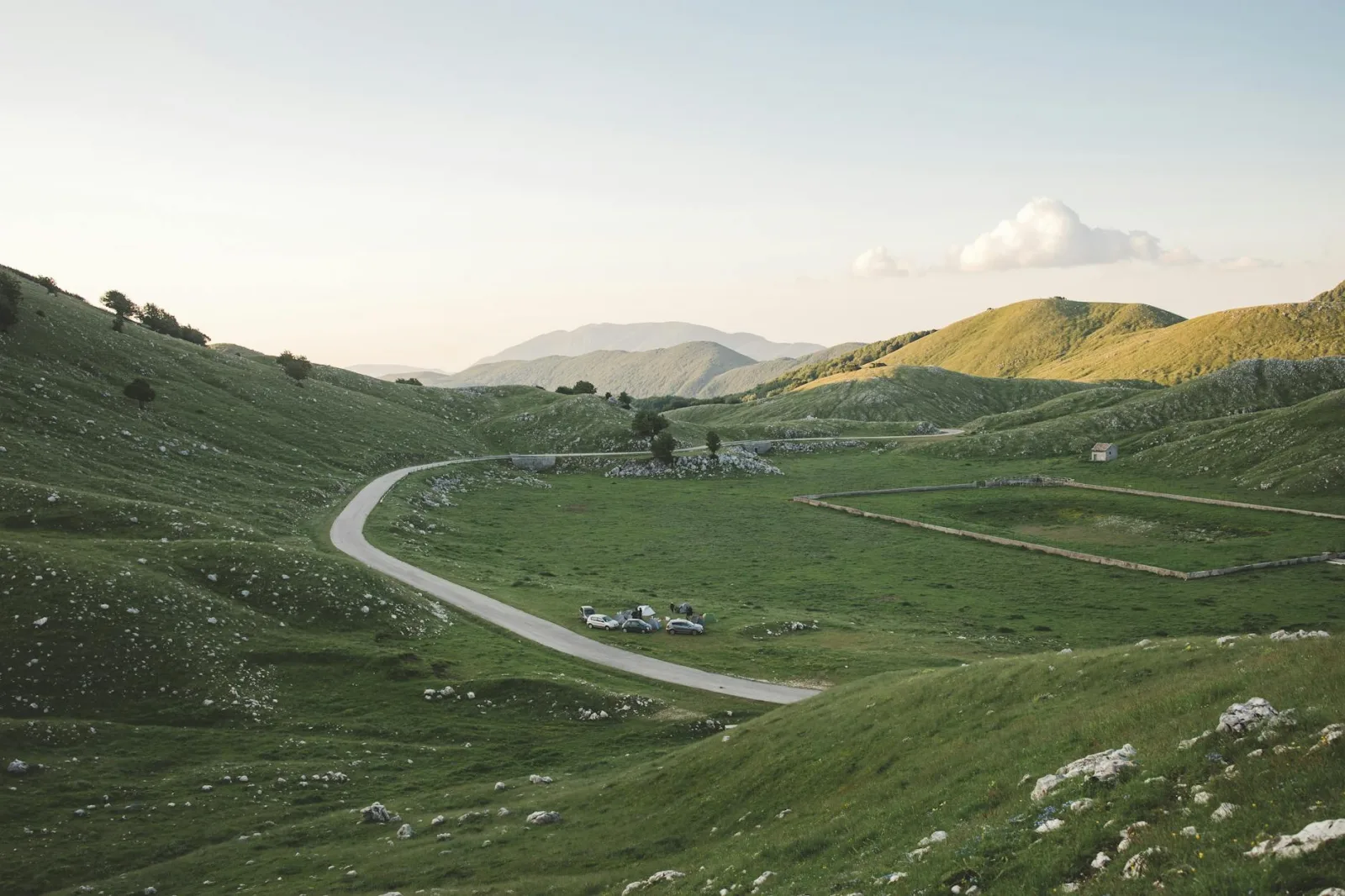 A picturesque view of a lush green plateau with a winding road and distant mountains under a clear sky.