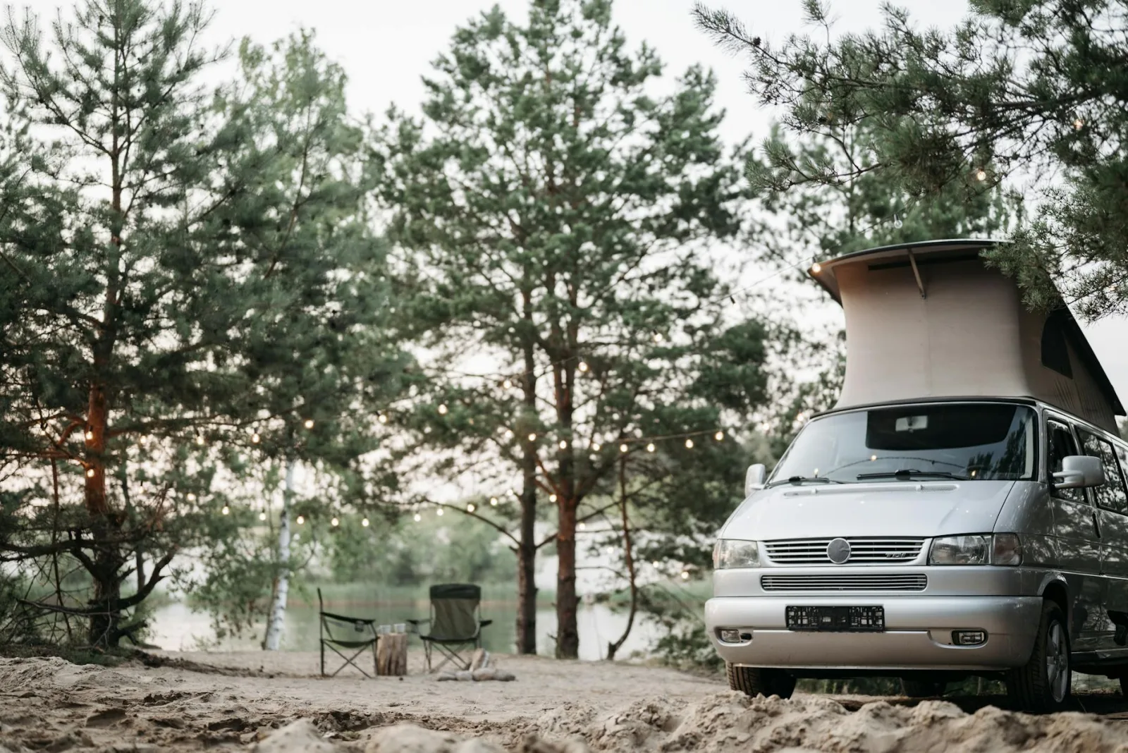 A serene camping scene with a camper van in a forest setting near a river, perfect for outdoor recreation and travel enthusiasts.
