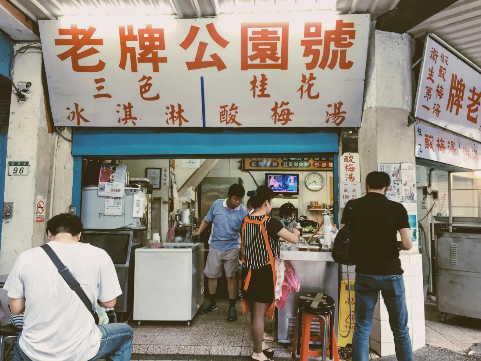 Vibrant street food stall with diverse customers in urban Asian city setting.