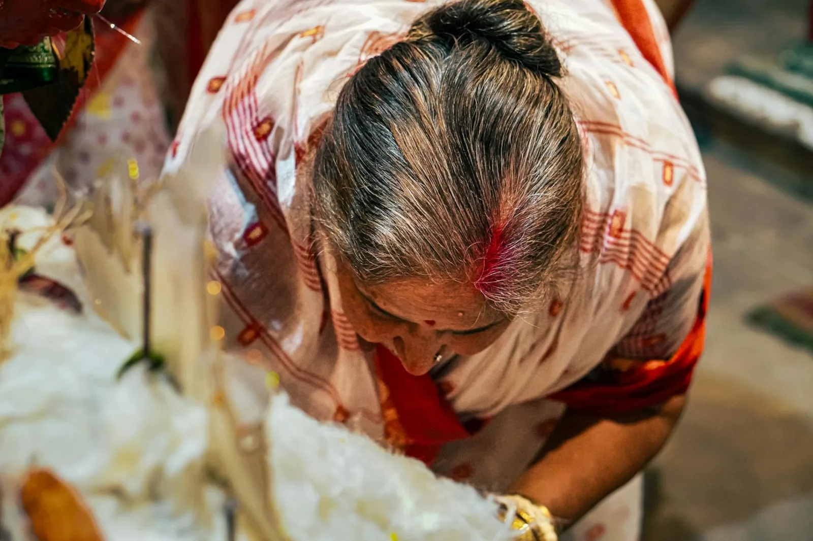 An elderly woman in traditional clothing participates in a cultural ritual ceremony.