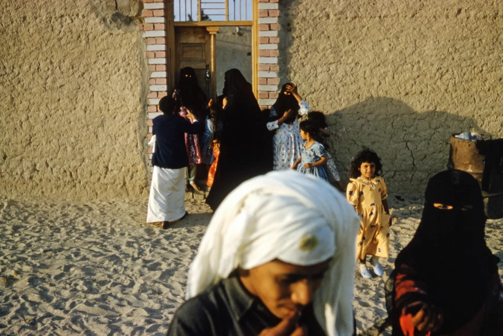 A group of people in traditional attire outside a desert village home.