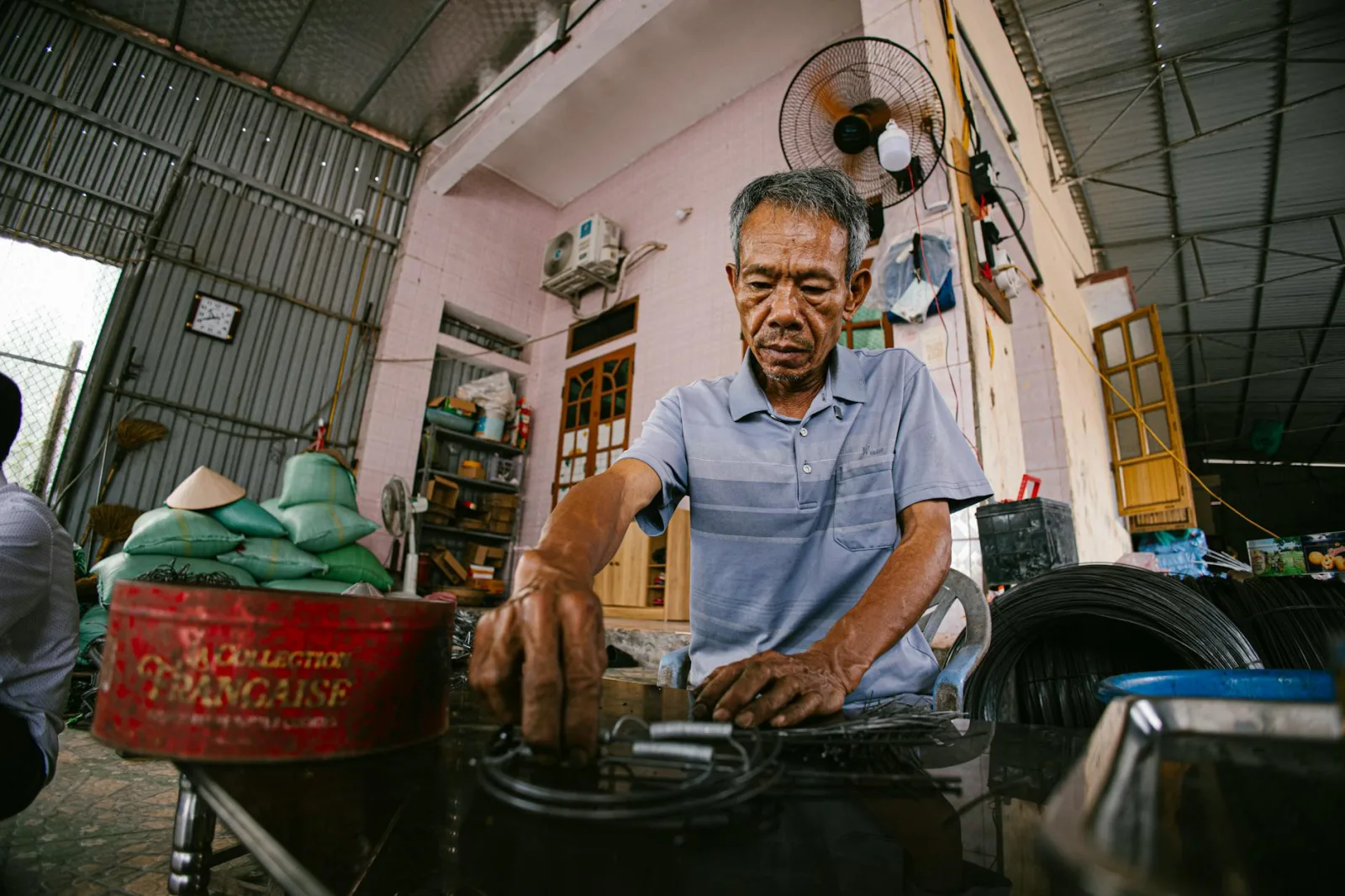 An elderly man focuses on his task in a bustling, industrial indoor workshop setting.