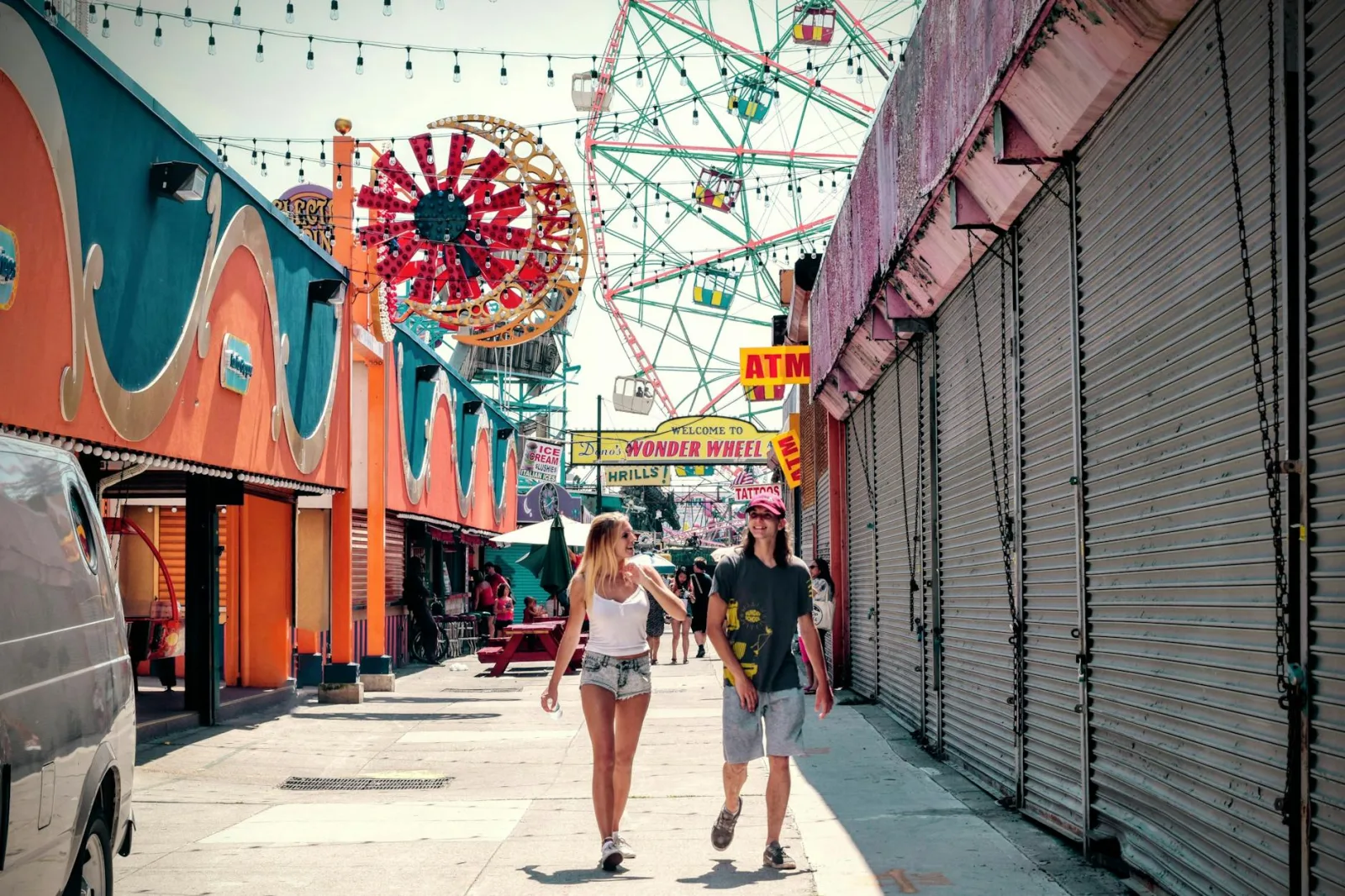 A couple enjoying a sunny day at an amusement park with colorful rides.