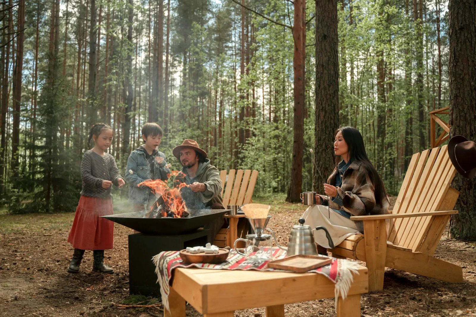 A family enjoying a camping trip with a fire pit in forest surroundings.