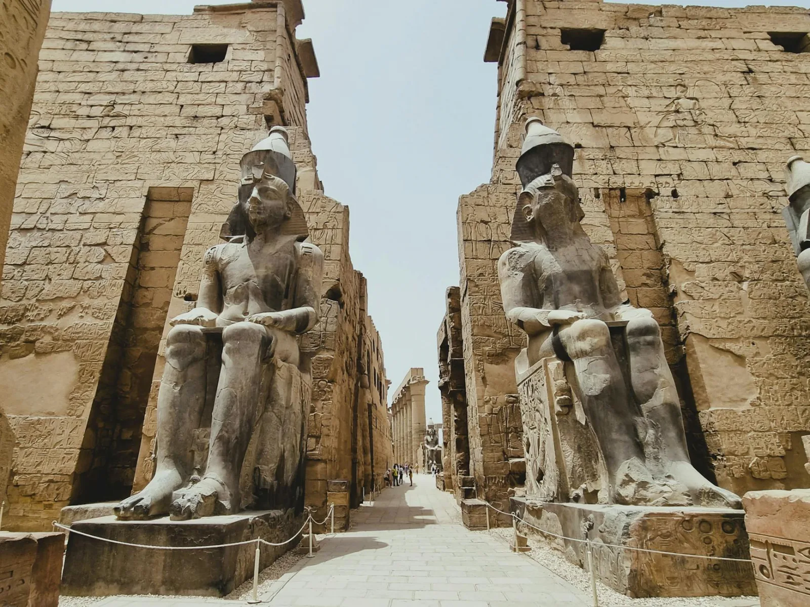 Explore the grandeur of ancient statues at the Luxor Temple entrance under a bright sky.