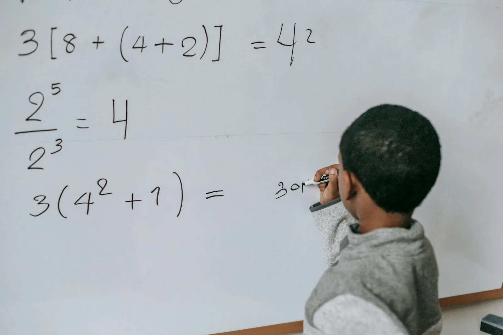 Focused child solving equations on a whiteboard, showcasing education and problem-solving skills.