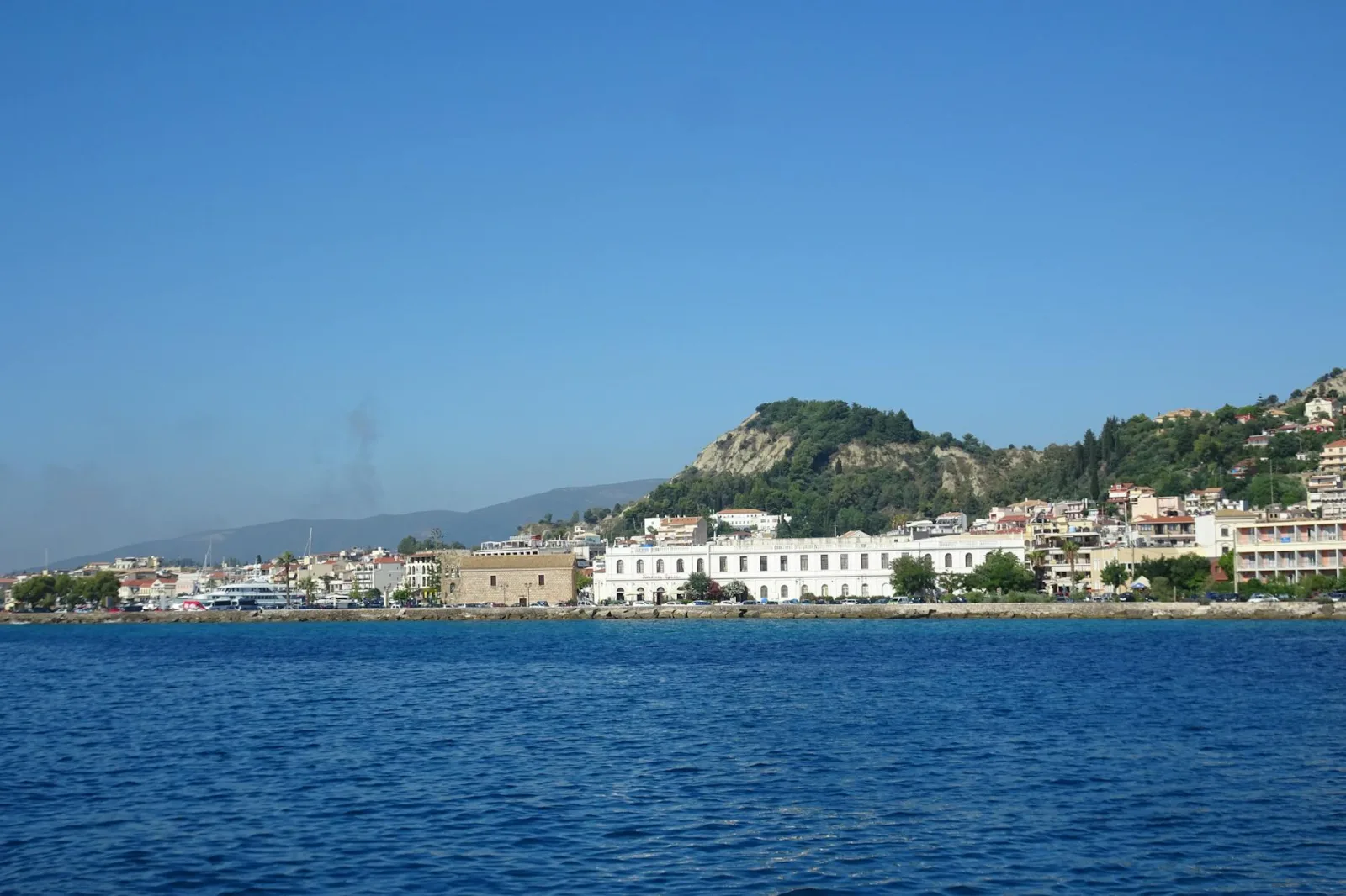 A serene view of a coastal Greek town with calm blue waters and a clear blue sky.