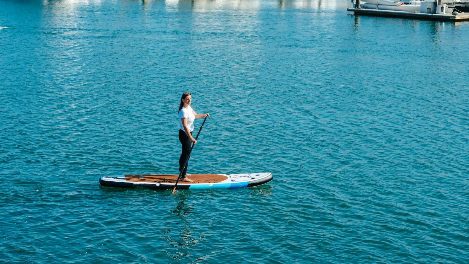 A woman enjoying paddle boarding on calm sea waters under a bright summer sun.