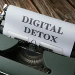 An overhead view of a typewriter printing 'Digital Detox' on wooden background.
