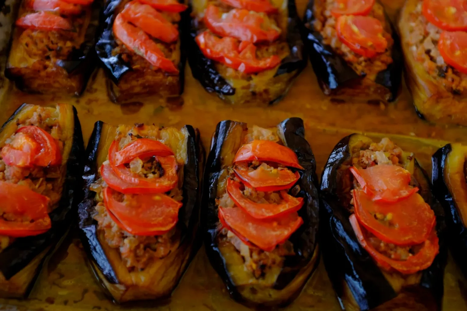 Baked eggplants stuffed with meat and topped with fresh tomatoes, perfect for Mediterranean cuisine lovers.
