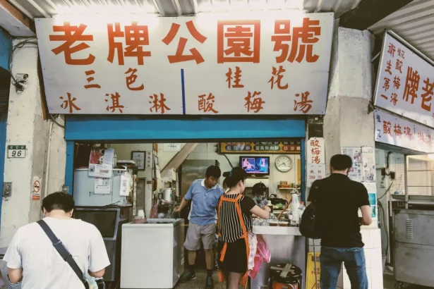 Vibrant street food stall with diverse customers in urban Asian city setting.