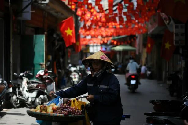 A vendor in a conical hat pushes a cart through a colorful street with red lanterns and flags.