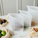 Reusable silicone and cloth bags storing lime, turmeric, and grains on a kitchen table.