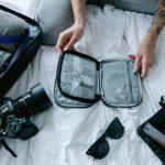 Traveler organizing essentials including a camera and packing cubes on a hotel bed.