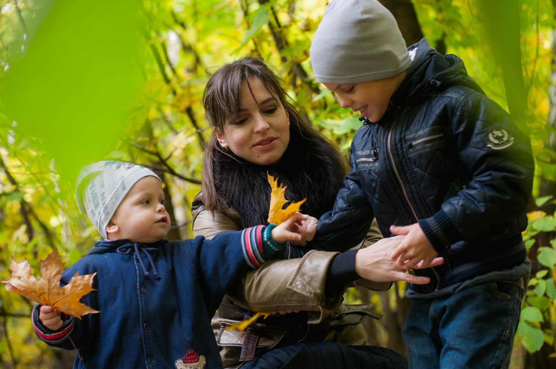 Joyful family moment in park with kids playing among colorful autumn leaves.