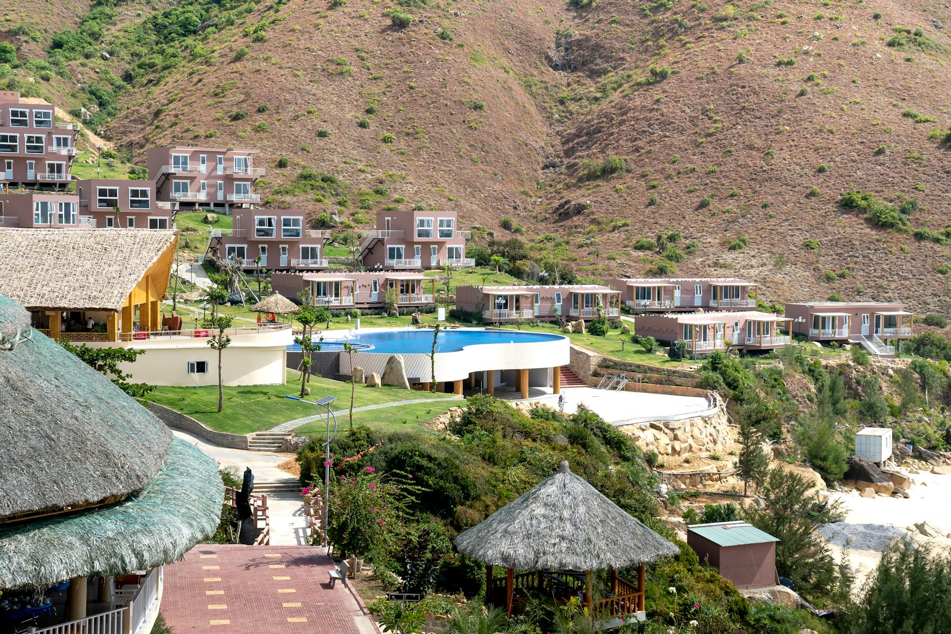 Remote settlement with contemporary villas and creative houses under straw roofs with outdoor pool located on hilly terrain on sunny day
