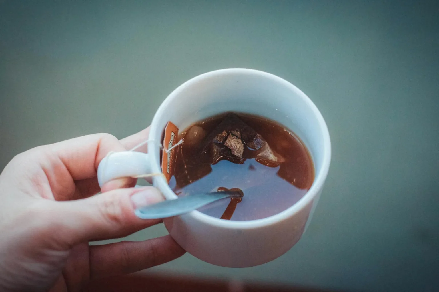 Elevated shot of a teacup with a tea bag and spoon in hand.