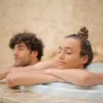 Happy cheerful man and woman with closed eyes bathing together leaning on bath edge during romantic weekend in luxury hotel in bathroom with marble interior