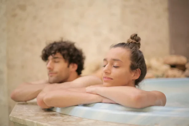 Happy cheerful man and woman with closed eyes bathing together leaning on bath edge during romantic weekend in luxury hotel in bathroom with marble interior