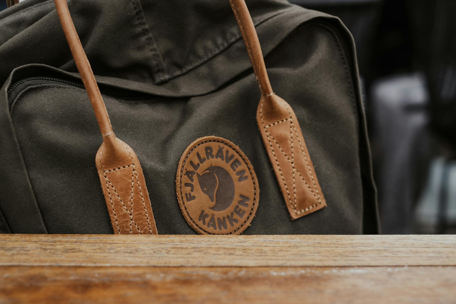 Stylish Fjällräven Kånken backpack featuring leather straps and logo detail on wooden table.