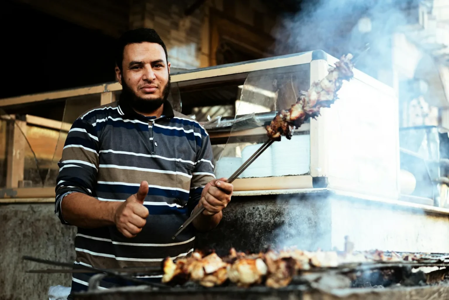 Street vendor in Cairo grilling delicious meat skewers on an outdoor barbecue.