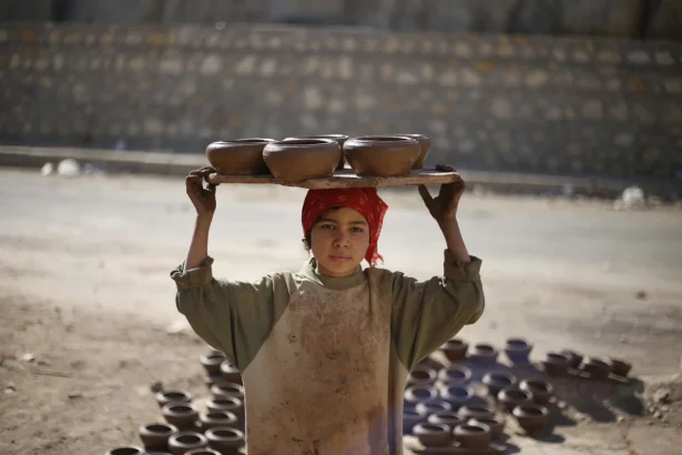 A child craftsman in Cairo carrying handmade pottery outdoors.
