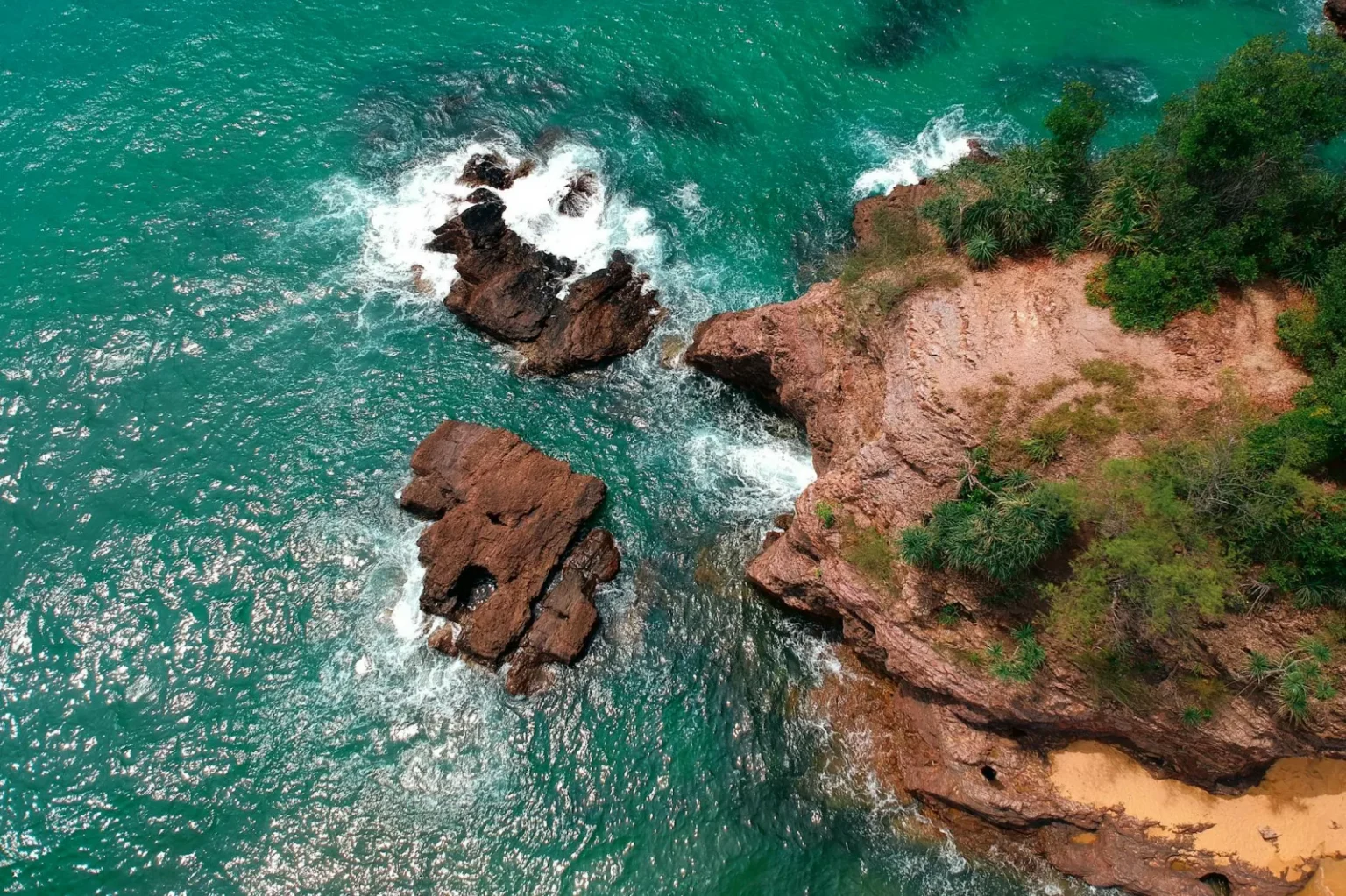Stunning aerial shot of a rocky tropical coastline with turquoise waters and lush greenery.