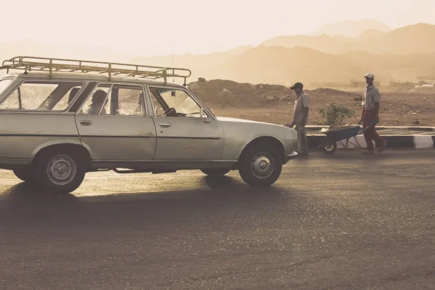 A classic Peugeot car with people walking by in Egypt's scenic desert sunset.